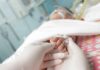 Gloved hands holding a baby's hand in a hospital bed