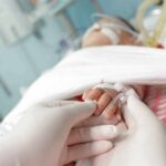 Gloved hands holding a baby's hand in a hospital bed