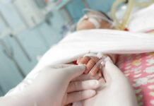 Gloved hands holding a baby's hand in a hospital bed
