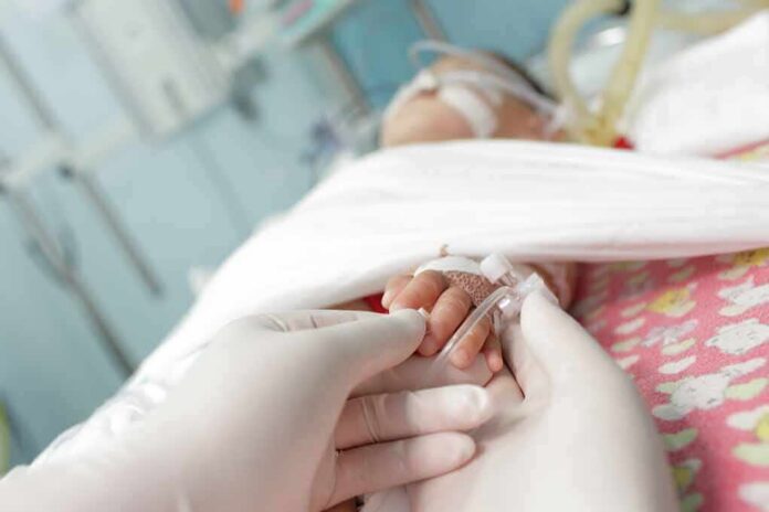 Gloved hands holding a baby's hand in a hospital bed