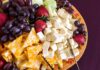 A colorful cheese and fruit platter featuring various cheeses and fresh fruits