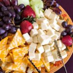 A colorful cheese and fruit platter featuring various cheeses and fresh fruits