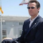 Tariff Blame Brawl Blows Up man in suit wearing sunglasses outdoors