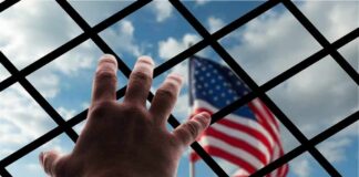 Hand reaching through fence toward blurred American flag