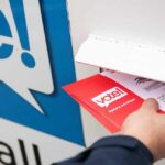 Last-Minute Mail Rule SMACKDOWN Hand inserting mail-in ballot envelope into drop box