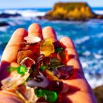 Hand holding colorful sea glass at a rocky ocean shore