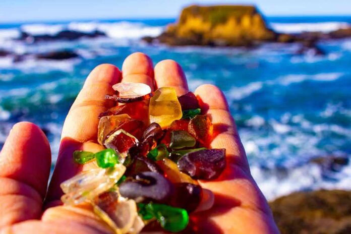 Hand holding colorful sea glass at a rocky ocean shore