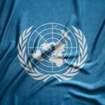 U.S. Slams UN Door Shut United Nations flag featuring a world map and olive branches on a blue background