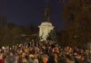 Crowd holding candles around a large statue at night