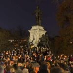 Crowd holding candles around a large statue at night