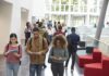 Students walking through a bright campus atrium using mobile devices