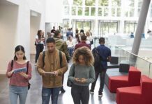 Students walking through a bright campus atrium using mobile devices