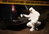 forensic investigator at car trunk behind crime scene tape