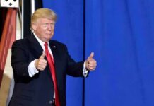 Donald Trump giving two thumbs up in front of a blue curtain