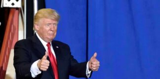 Donald Trump giving two thumbs up in front of a blue curtain