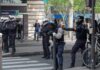 Riot police in helmets line a city street during an operation