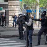 Riot police in helmets line a city street during an operation