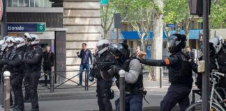 Riot police in helmets line a city street during an operation