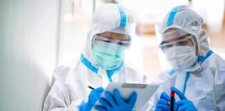 Two healthcare workers in full PPE reviewing a clipboard