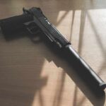 Black pistol with suppressor on wooden table