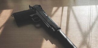 Black pistol with suppressor on wooden table