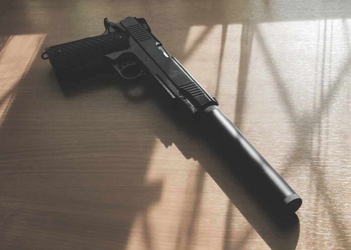 Black pistol with suppressor on wooden table