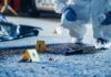 Forensic investigator examines a crime scene with evidence markers and a handgun