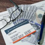 Medicare card on paperwork with cash, glasses, and a pen
