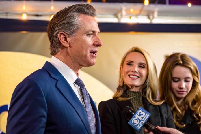 Man in a blue suit speaks to reporters while two women stand beside him