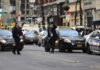 Police officers manage a taped-off city street with patrol cars and bystanders