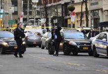 Police officers manage a taped-off city street with patrol cars and bystanders