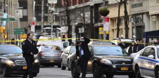 Police officers manage a taped-off city street with patrol cars and bystanders