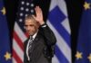 Barack Obama waves on stage with flags in the background