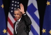 Obama Rescue Mission in Detroit? Barack Obama waves on stage with flags in the background