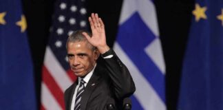Barack Obama waves on stage with flags in the background
