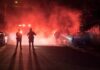 Police officers watch firefighters extinguish a car fire at night