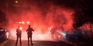 Police officers watch firefighters extinguish a car fire at night